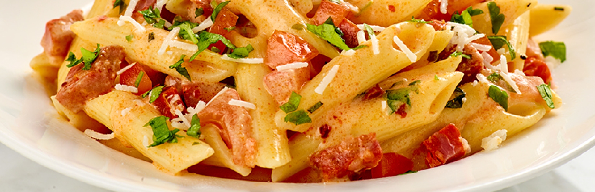An image of a bowl of penne pasta, tomatoes and chorizo with a bowl of cooking cream in the background