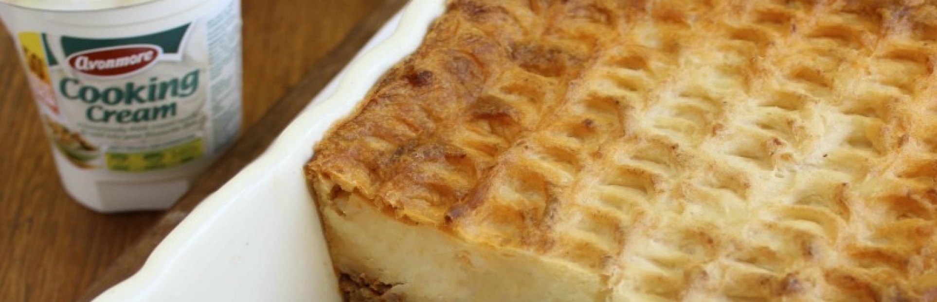 An image of a baked cottage pie with a pot of cooking cream beside it 
