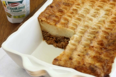 An image of a baked cottage pie with a pot of cooking cream beside it 